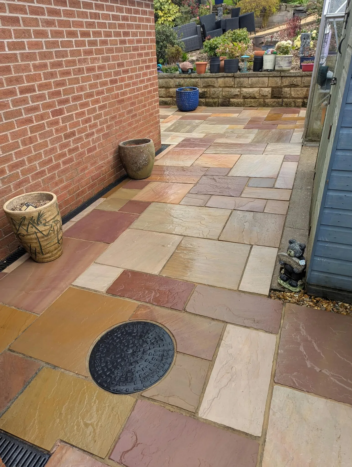 Clean paved path beside the brick house and blue shed, still wet after cleaning.