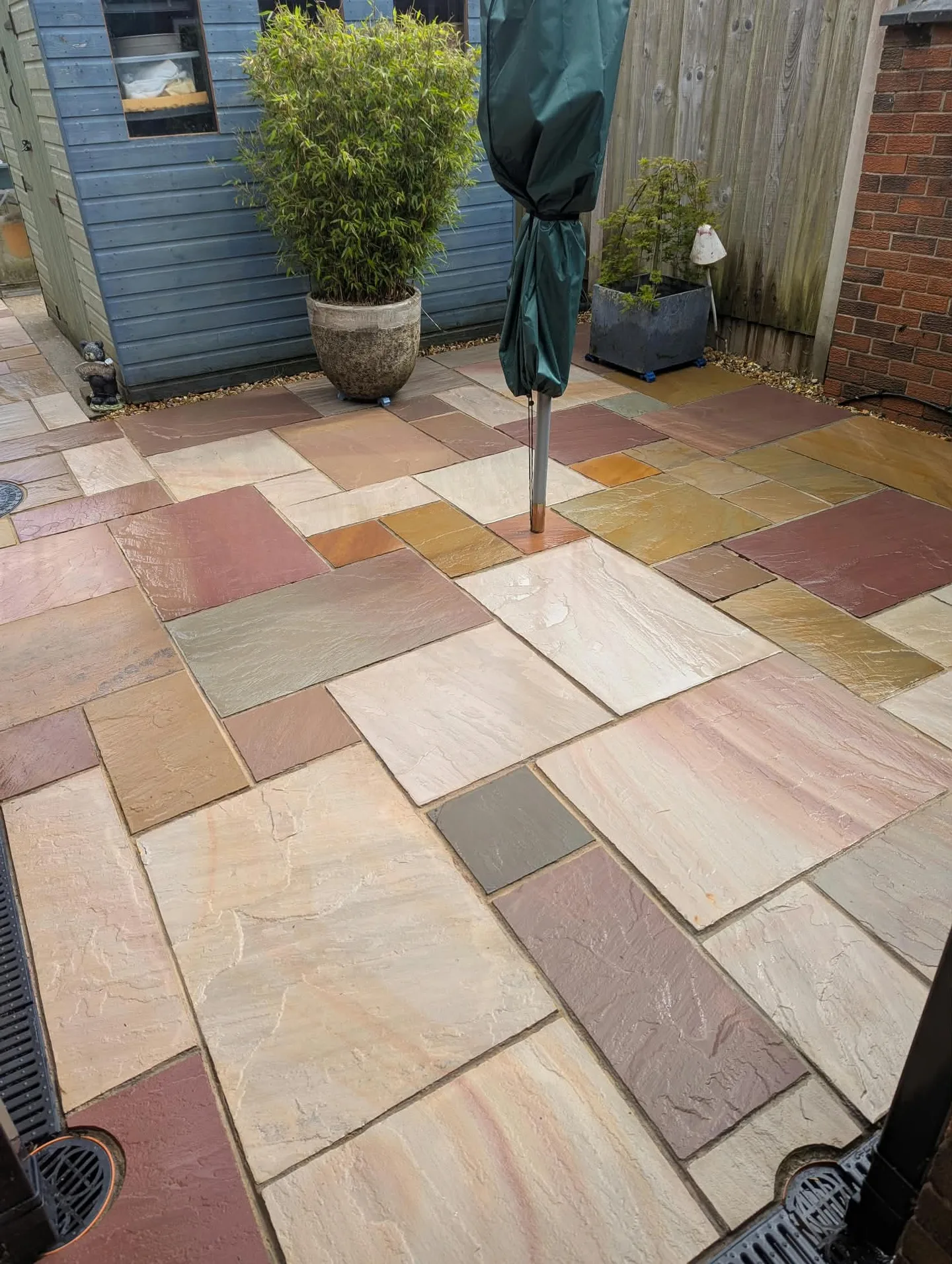 Clean patio paving around the covered parasol and plant pots, still wet after cleaning.