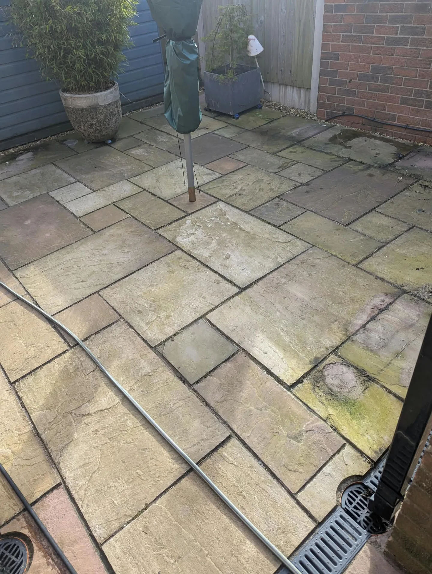 Patio paving around a covered parasol and plant pots before cleaning.