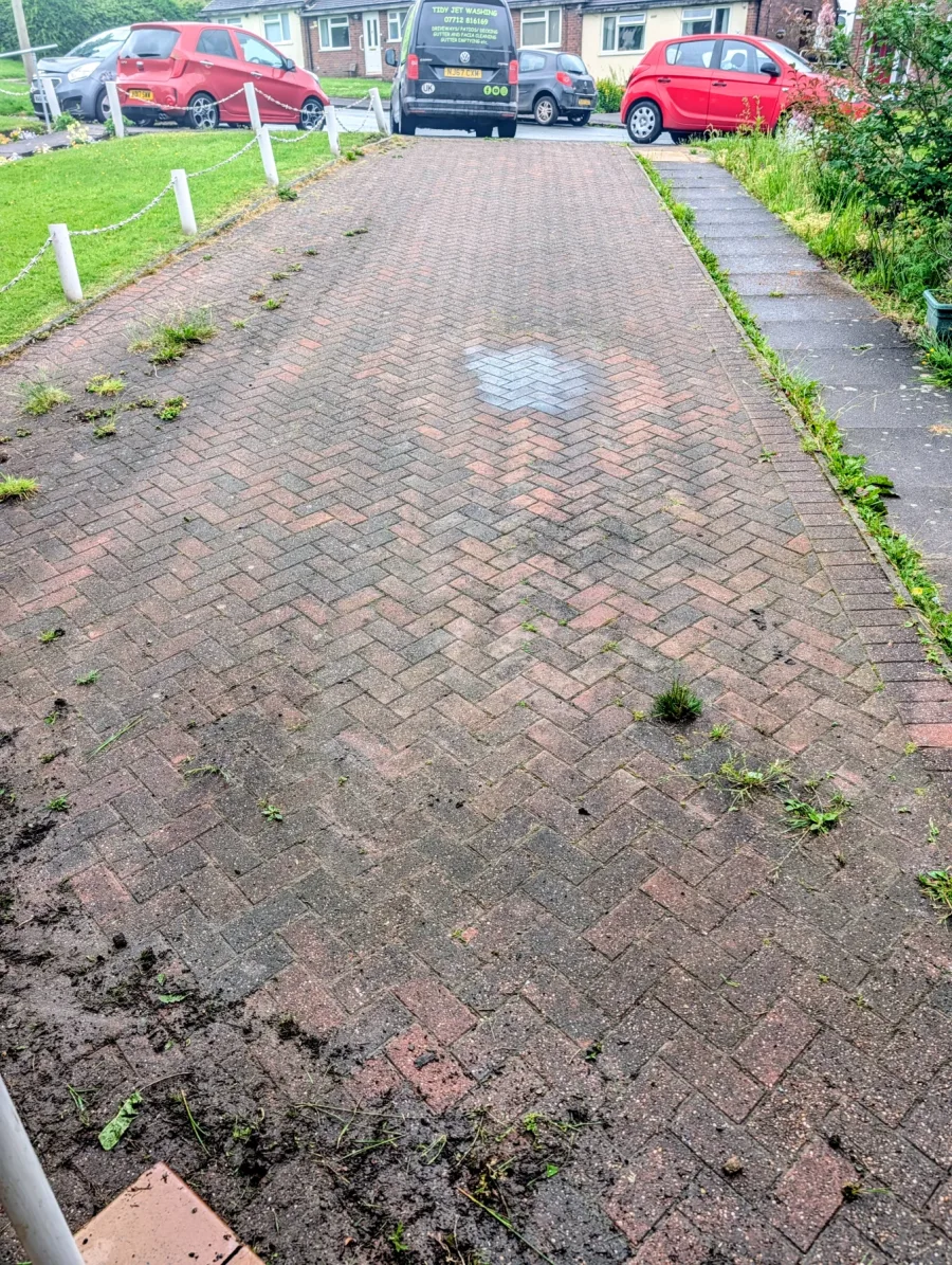 A front block-paved driveway with weeds and organic build-up before cleaning