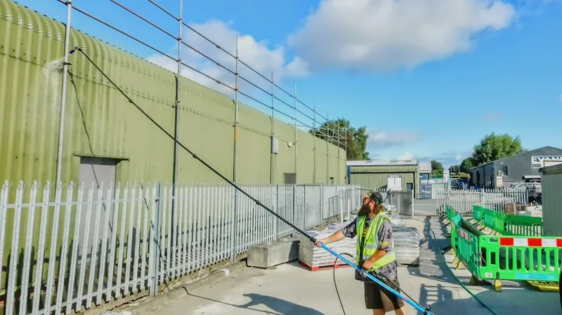 Mike cleaning cladding on a commercial industrial unit using long-reach equipment.