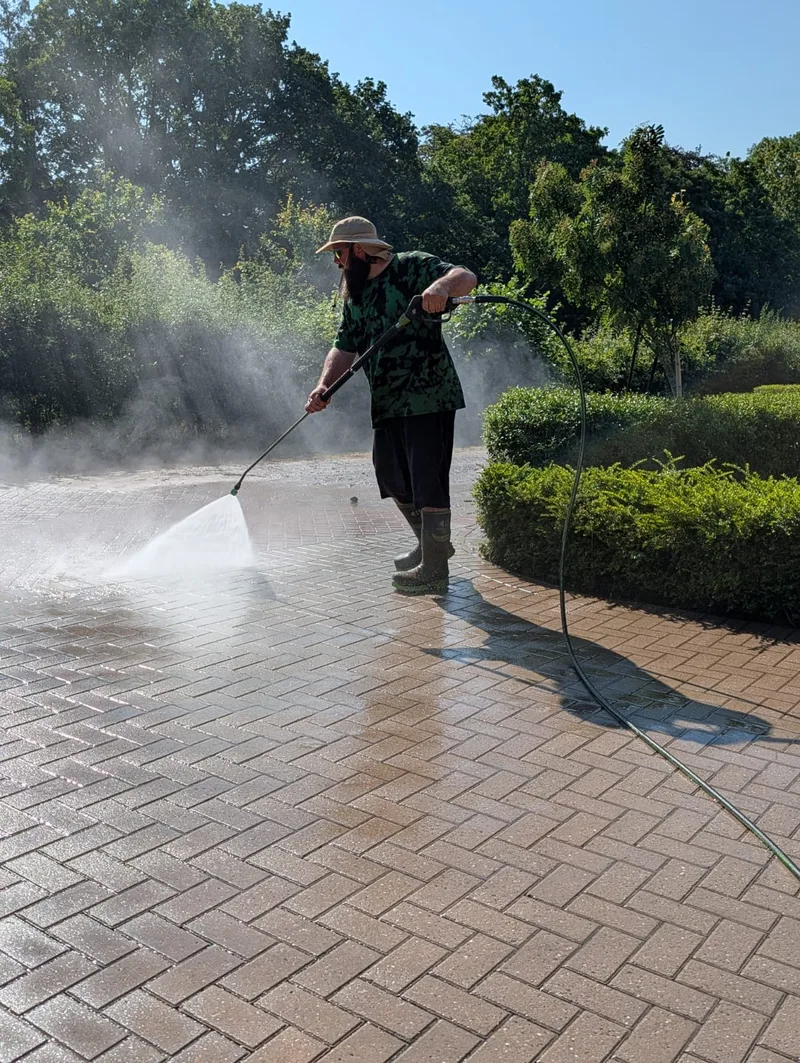 Jet washing a block-paved driveway in bright daylight.