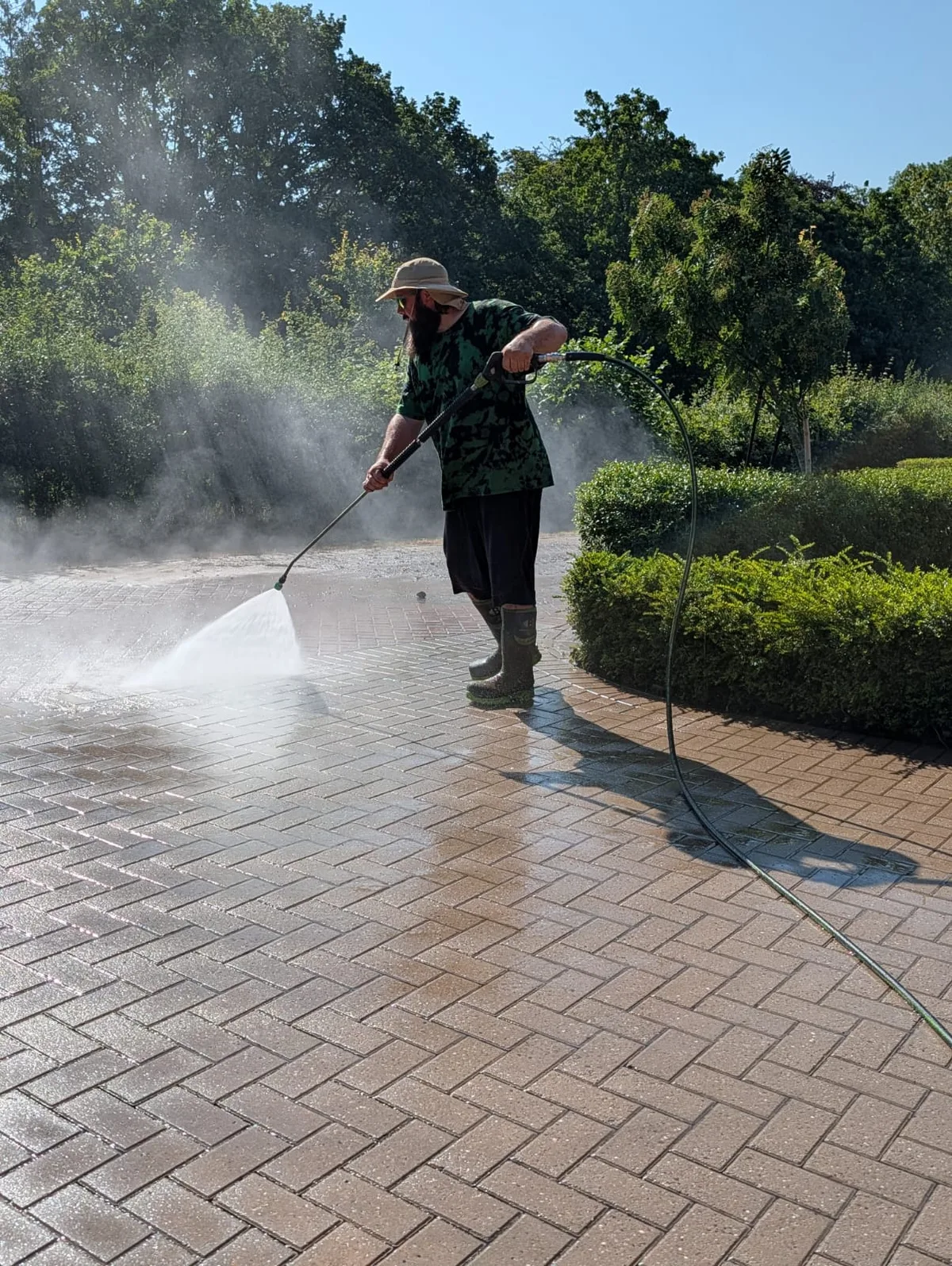 Jet washing a block-paved driveway in bright daylight.