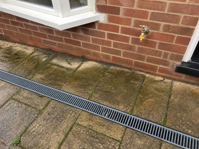 Close photograph showing only a small area of stained paving beside a wall.